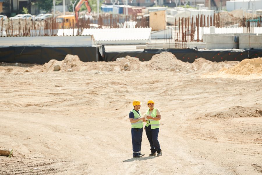 Two workers in hard hats and safety vests on a job site